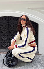 Side view of cream knit jacquard track pants, showing the relaxed fit, dark blue side stripe, and ribbed ankle cuffs