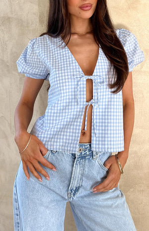 Close up of girl wearing a blue gingham tie up top, blue denim jeans and gold jewellery.
