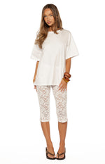 Front view of white floral lace mid-rise capri pants with small side slits at the hem
