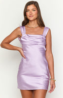 blonde model wearing a lilac satin mini dress paired with gold bracelets and gold hoop earrings