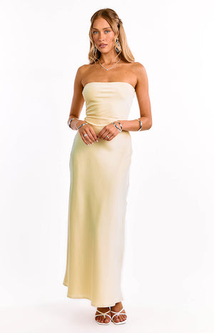 A model in a yellow strapless maxi dress with an elegant straight neckline. This sophisticated formal dress features a sleek column silhouette. An ideal choice for a wedding guest or graduation ceremony.