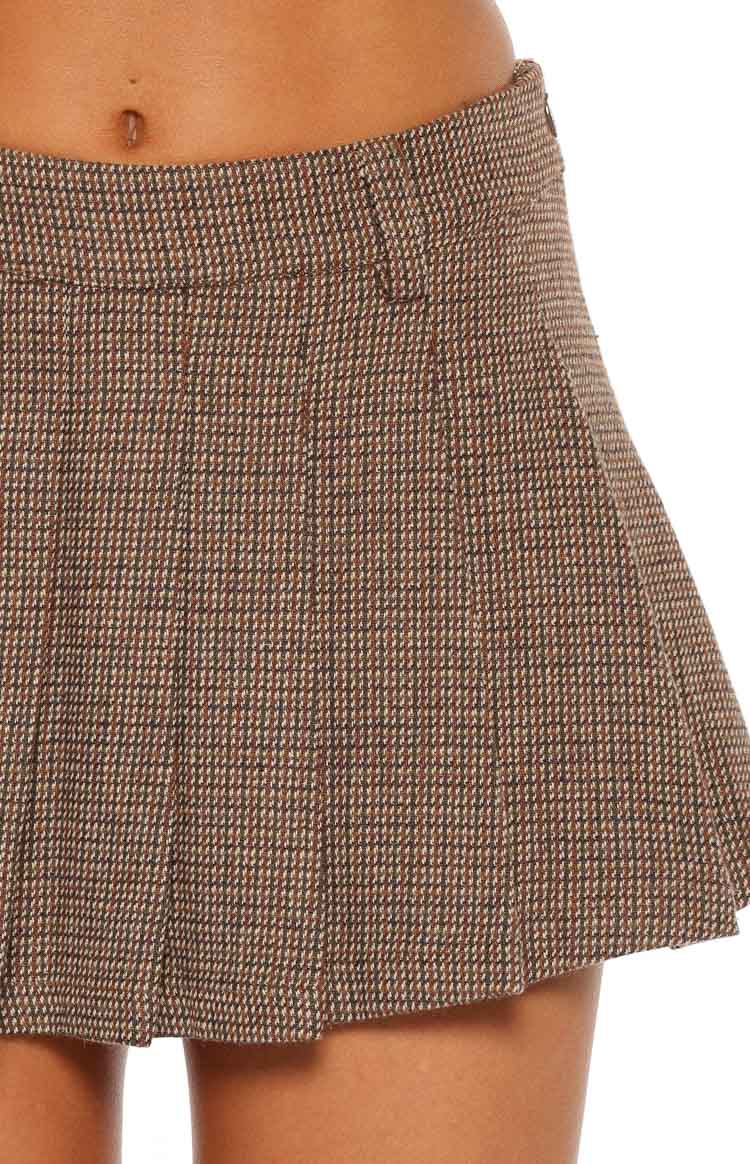 Close-up of the brown herringbone fabric of a mini skirt, showing the fine pattern and pleated detail