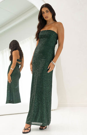 Our model wearing a strapless maxi gown in a shimmering emerald green color. This entire maxi is covered in vertical lines of fine glistening sequins giving it a sparkling texture and a straight column silhouette. A reflection in the mirror shows a cut-out detail on the back of the maxi dress.