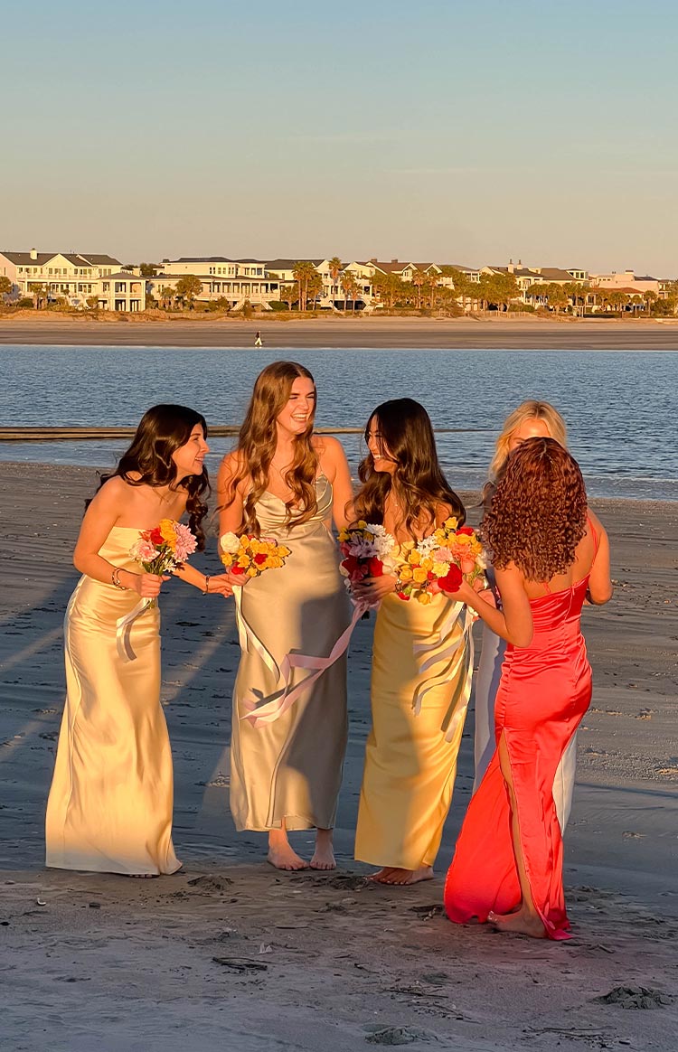Strapless satin midi dresses in yellow, light green, coral, and white on a beach
