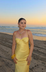 Full length view of a yellow satin midi dress with a lace-trimmed sweetheart bust and thin spaghetti straps beach