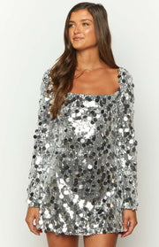 Square neckline and long sleeves of a silver mini dress, adorned with large, shimmering sequins