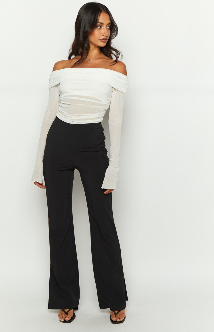 A full length studio shot our model wearing high-waisted black trousers with a slim fit through the hips and a wide-leg silhouette.