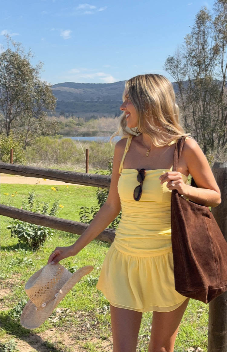 Side view of a yellow mini dress with a ruched bodice, tie-shoulder straps, and a flowy skirt
