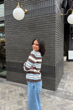 Side view of a relaxed fit brown, blue, and white striped knit cardigan with ribbed cuffs and hem