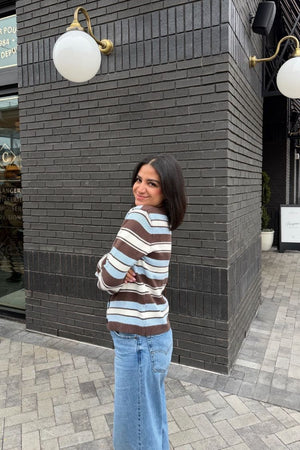 Side view of a relaxed fit brown, blue, and white striped knit cardigan with ribbed cuffs and hem