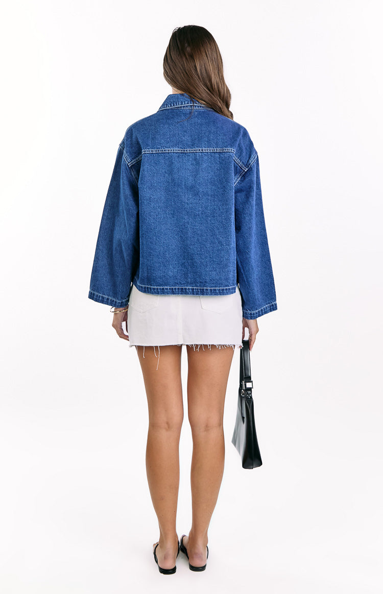Rear view of a mid wash denim jacket with white contrast stitching, a classic collar, and wide long sleeves