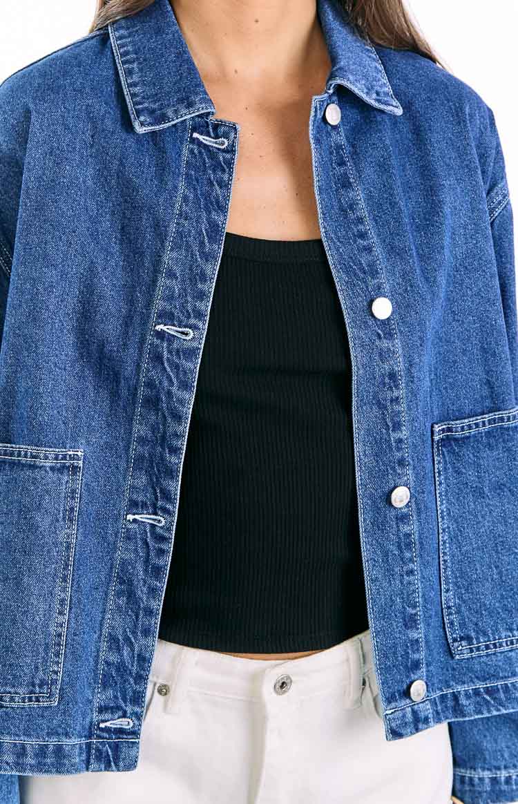 Close-up of the mid wash denim jacket, open, showing the collar, white buttons, and contrast stitching