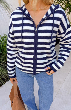 A knit, zip-up hoodie with navy blue and white horizontal stripes, featuring a drawstring hood and a relaxed fit.