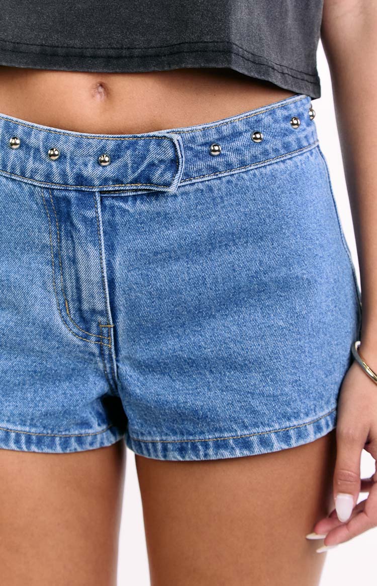 Close-up of mid wash blue denim low rise shorts showing the front fly and silver studs along the waistband
