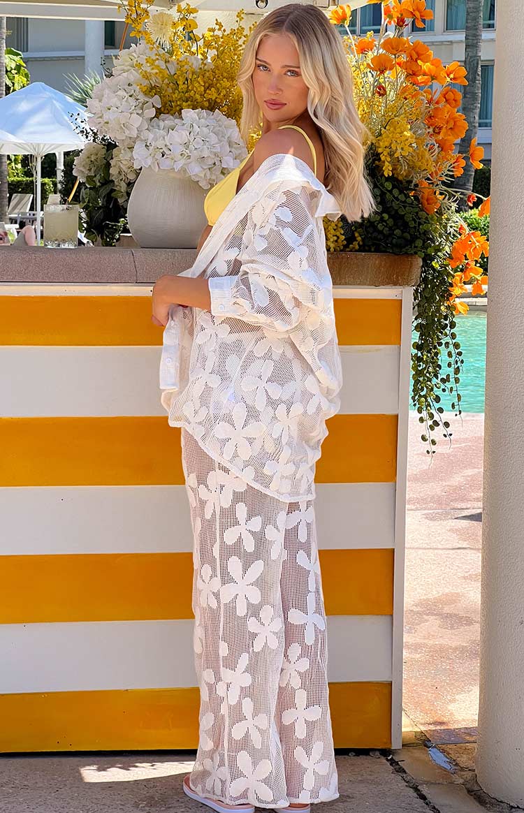Side view of white wide-leg pants with a sheer floral mesh pattern, showing the relaxed fit