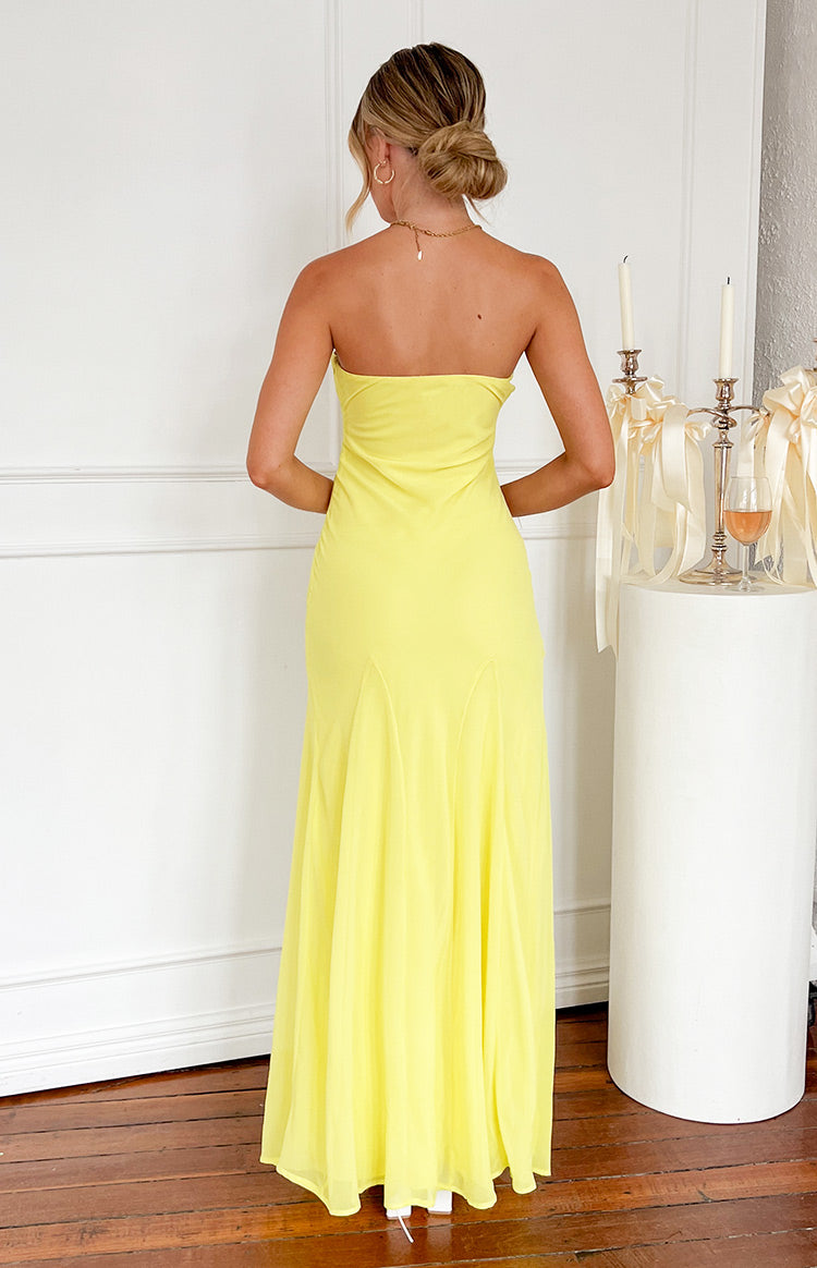 Back view of the yellow strapless maxi dress with a straight back neckline and a flowing skirt featuring subtle panel details