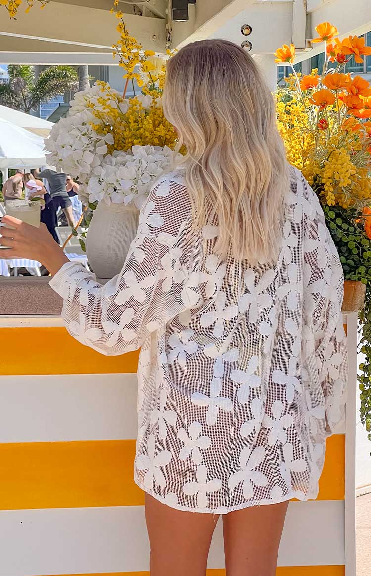 Back view of a white long sleeve mini dress in a sheer floral open-knit fabric, showing the relaxed fit