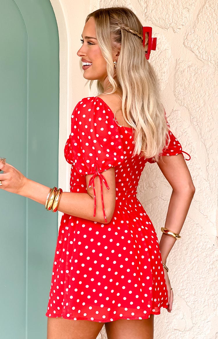 Side view of a red polka dot mini dress with a square neckline, short tie-up puff sleeves, and shirred waist