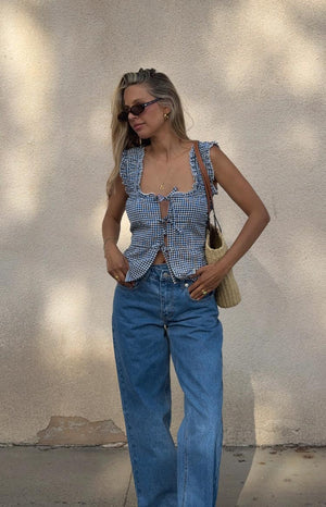 Girl wearing a black and white gingham tie-front top. This full outfit view shows the top styled with wide-leg denim jeans and a woven tote bag.