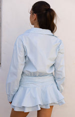 Rear view of a light blue long sleeve mini shirt dress with a gathered elasticated waist and tiered ruffled hem