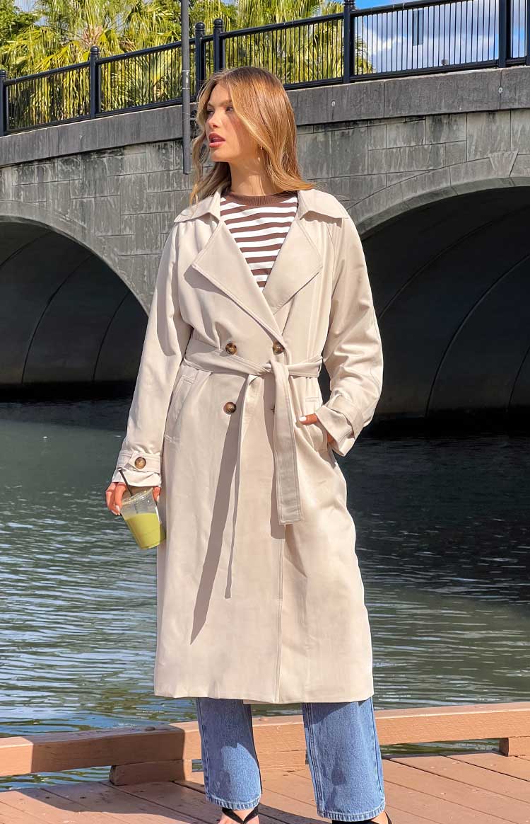 Cream trench coat with wide lapels, double-breasted front, and a self-tie belt cinching the waist