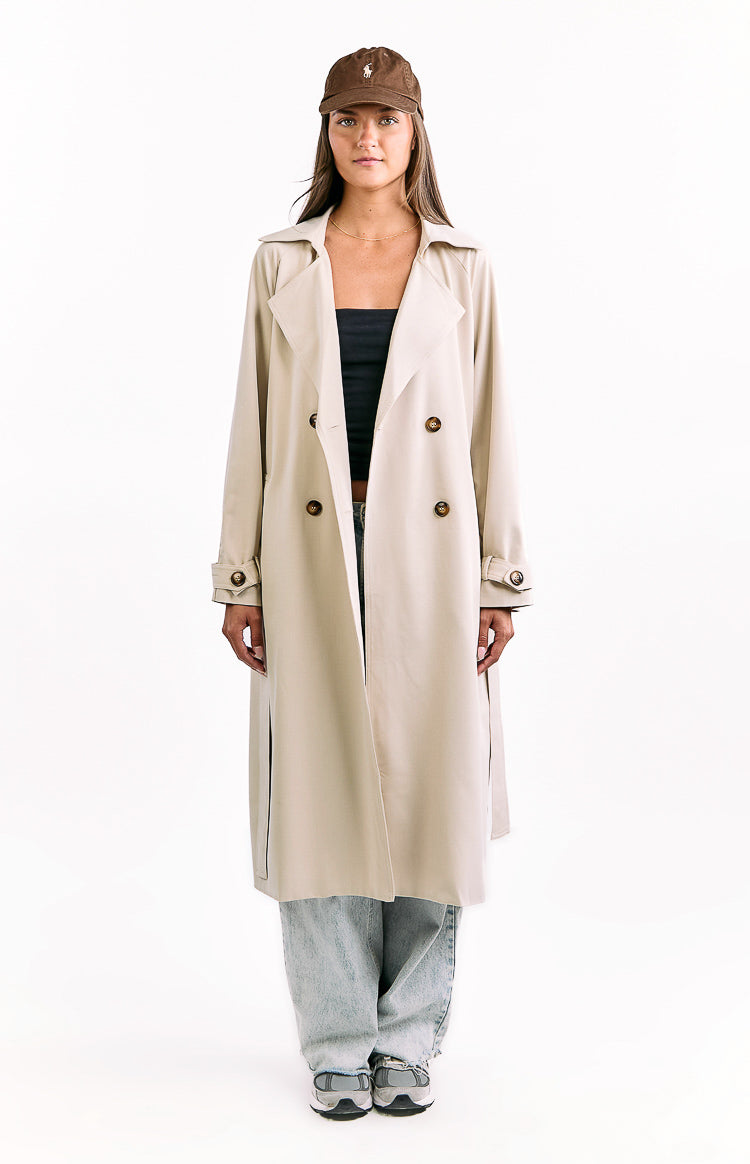 Cream trench coat worn open, showing wide lapels, double-breasted buttons, long sleeves with cuff straps, and side slits