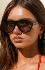 Close-up of black aviator sunglasses with dark tinted lenses and OTRA logo on the temple