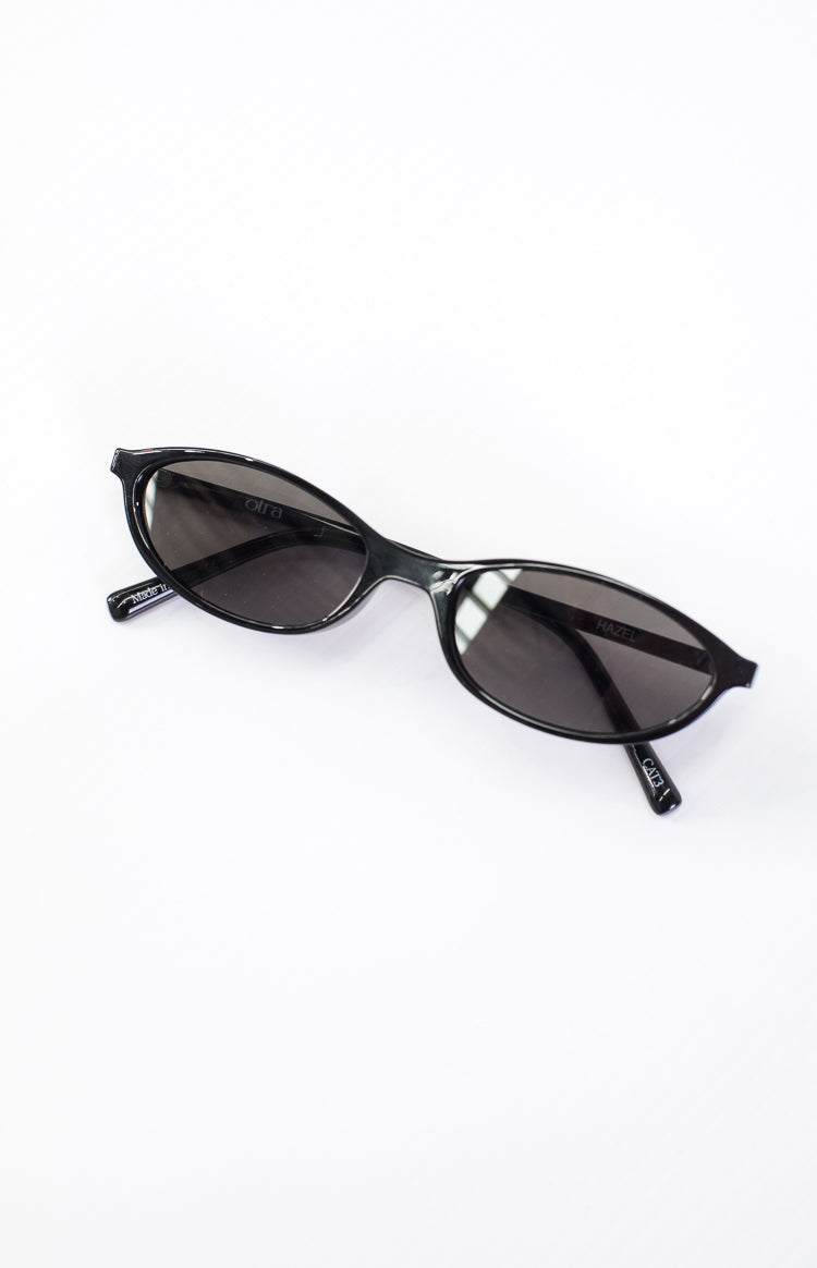 Angled overhead view of black cateye sunglasses with "otra" on left lens and "HAZEL" on right lens, "CATE3" on arm