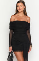 Brunette model wearing a black long sleeve off shoulder mini dress and gold jewellery holding a drink.