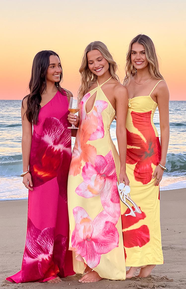 Flowy hot pink one-shoulder maxi dress with a large dark orchid print, flowing to the sand