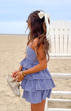 Girl wearing a blue and white gingham mini dress with tiered ruffle layers through the bodice