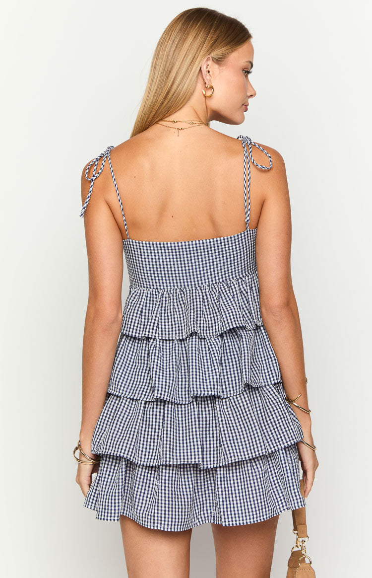 Back view of a navy gingham mini dress showing tie-shoulder straps and a smocked bodice above tiered ruffles