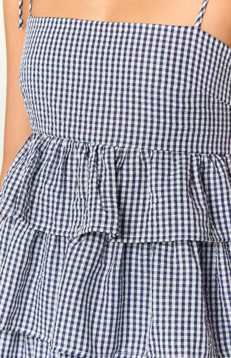 Detail of the navy gingham dress with a fitted bodice, gathered waist seam, and the first tier of the ruffled skirt