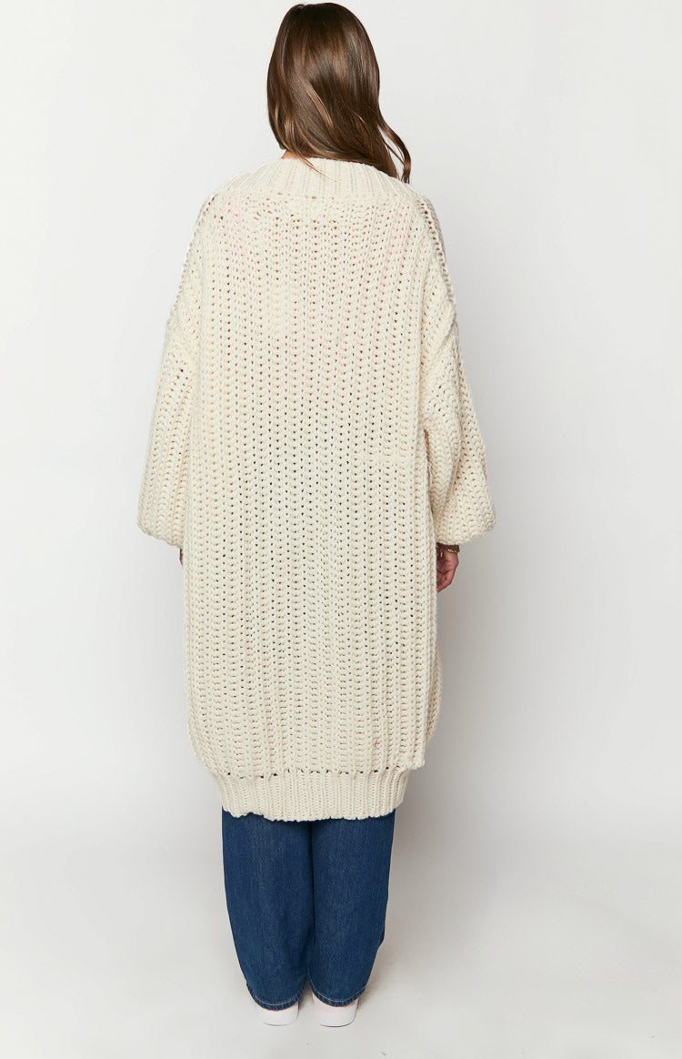 Rear view of a cream chunky knit longline cardigan with an open stitch pattern and wide sleeves
