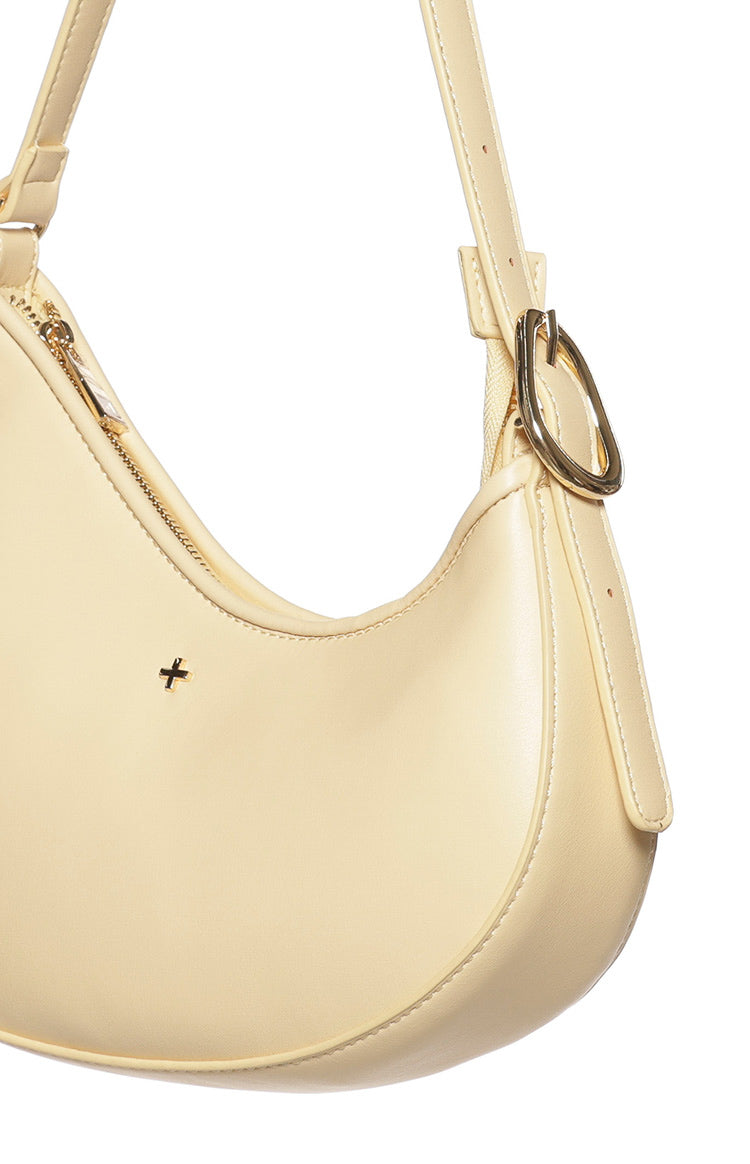 Close-up of the cinder yellow shoulder bag showing the gold zipper closure, plus logo, and adjustable strap buckle
