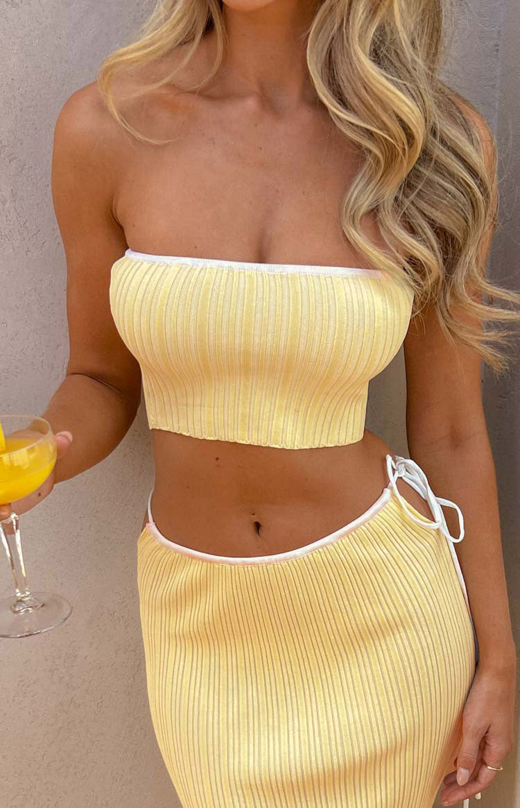 Mid-shot of a yellow ribbed knit tube top featuring white contrast binding on the strapless neckline and hem