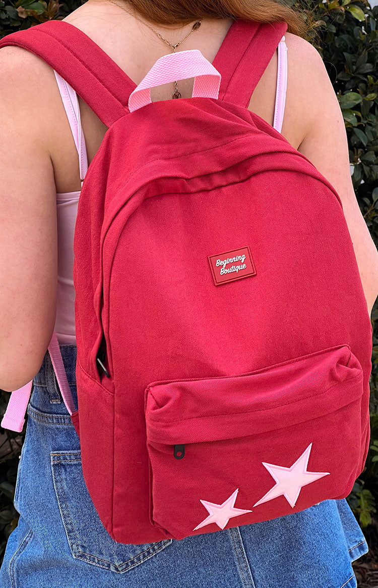 Rear view of a burgundy backpack with padded shoulder straps, a pink top handle, and pink star appliques