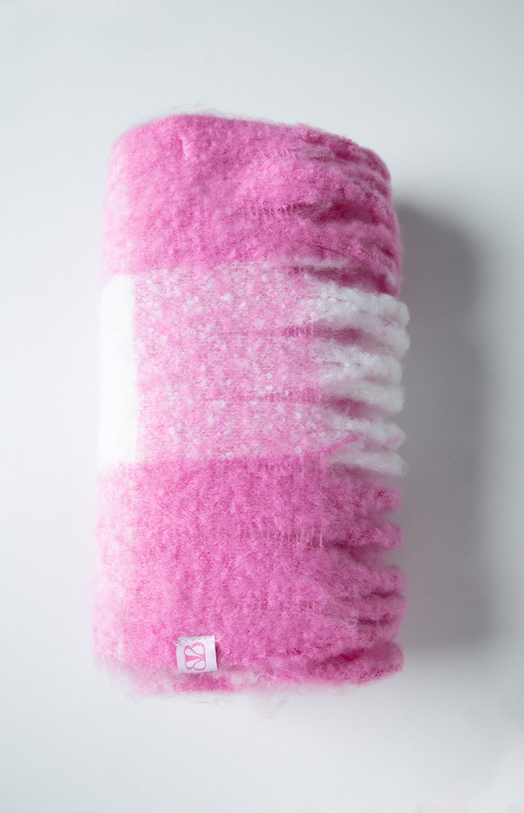 Rolled-up view of a pink and white fluffy blanket scarf with a white stripe and small brand tag