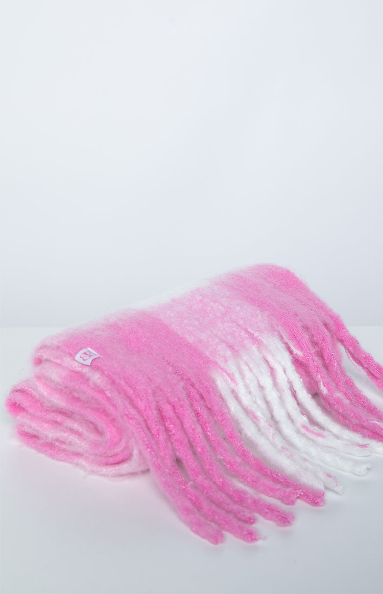 Close-up of a folded pink and white fuzzy blanket scarf with fringed ends and a small white label
