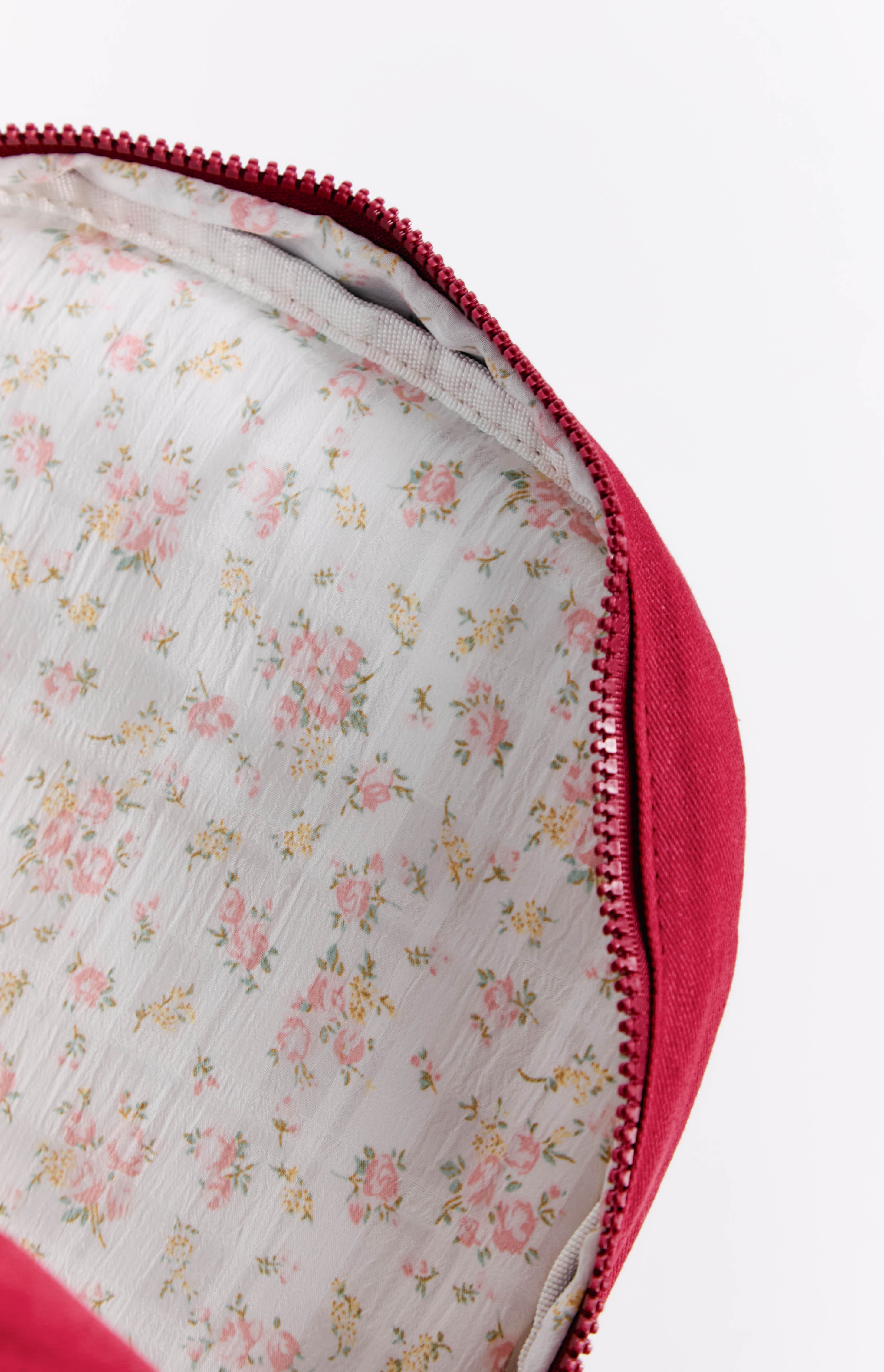 Close-up of the burgundy backpack interior, showing the white lining with pink and yellow floral pattern and zipper