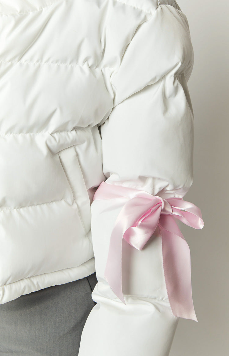 Close-up of the pink satin bow tied around the sleeve of a white puffer jacket