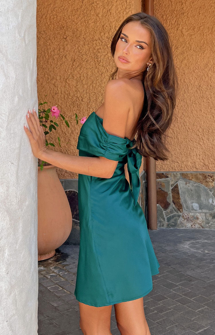 Side view showing the teal satin mini dress with ruched off-the-shoulder sleeves and a large tie-back bow