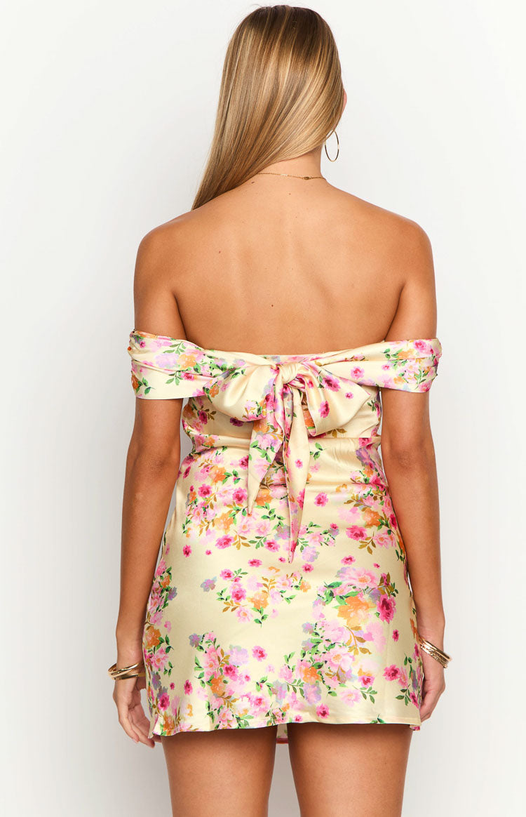 Back view of a primrose yellow floral off-the-shoulder mini dress with a large tie-back bow