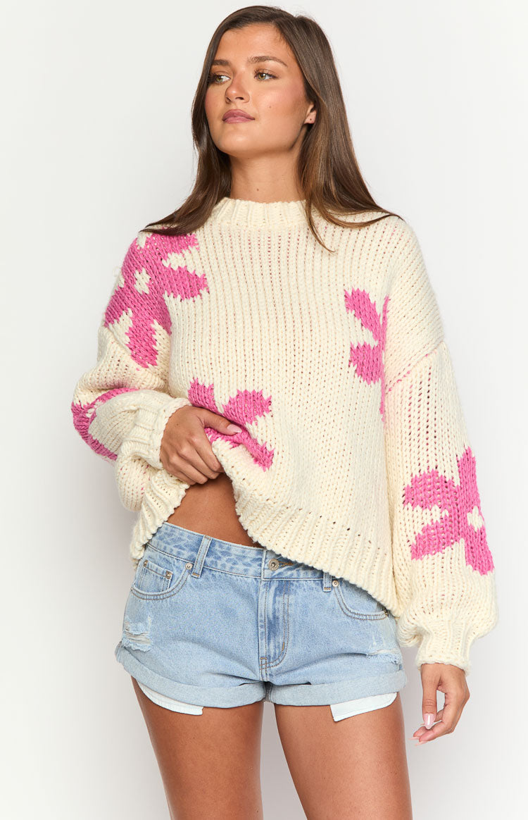 Close-up of the cream chunky knit sweater with large pink flower patterns, ribbed crew neck, cuffs, and hem