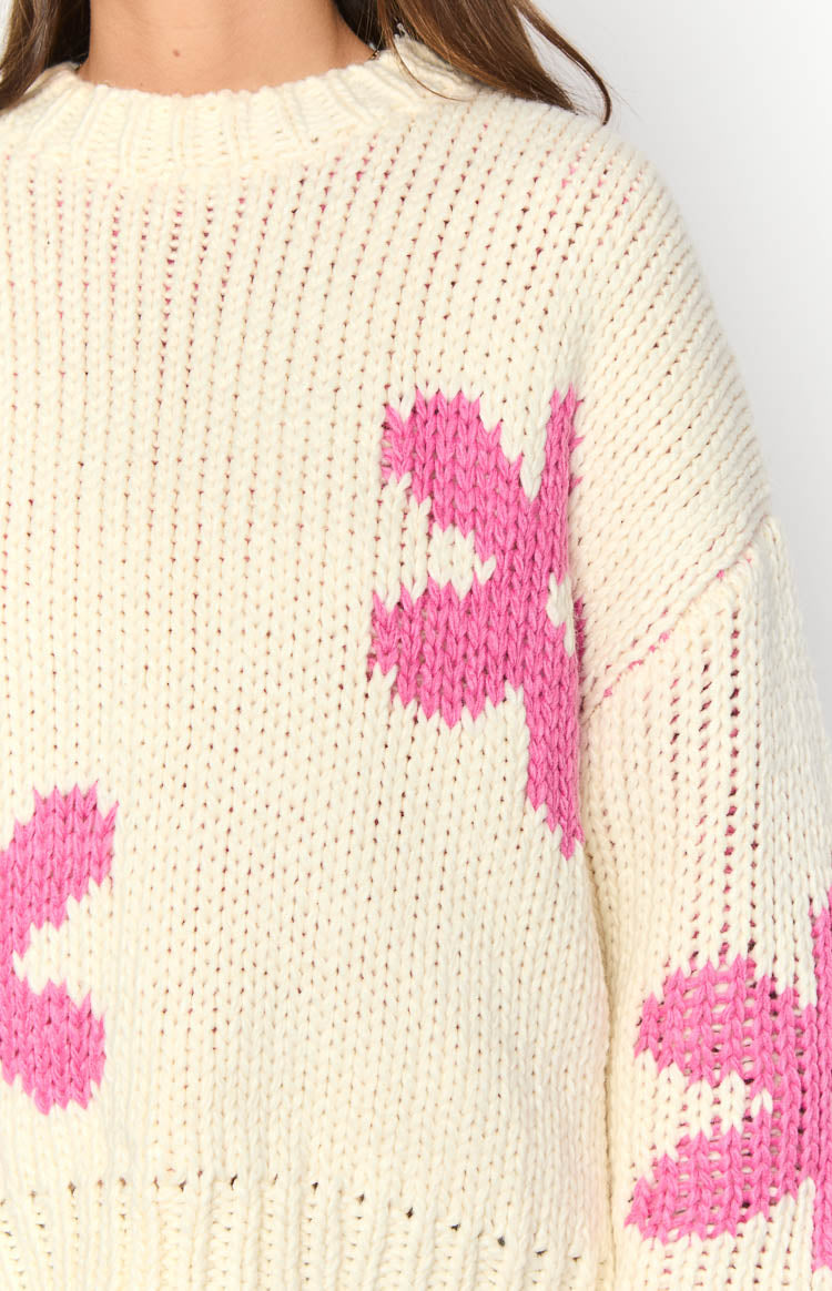Close-up of the cream chunky knit sweater with pink flower patterns on the shoulder and sleeve