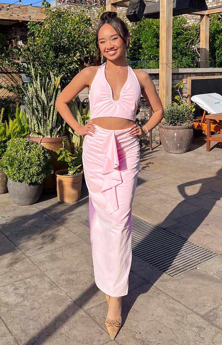 Front view of a pink halter neck maxi dress with a deep V-neck, cropped top, and ruched skirt with ruffle