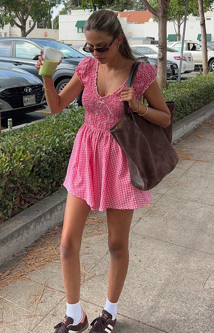 Red gingham playsuit with a smocked bodice, V-neckline with tie detail, short ruffled sleeves, and flowy shorts