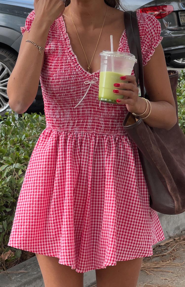 Close-up of the red gingham playsuit showing the shirred bodice, V-neck tie, ruffled cap sleeves, and gathered waist