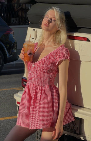 Red gingham playsuit with a V-neck, shirred bodice, short ruffled puff sleeves, and flowy shorts