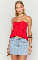 Model displays a vibrant red strapless ruffle top featuring a ruched drawstring front, paired with a light wash denim mini skirt and accessorised with chunky gold necklaces and stacked bangles.